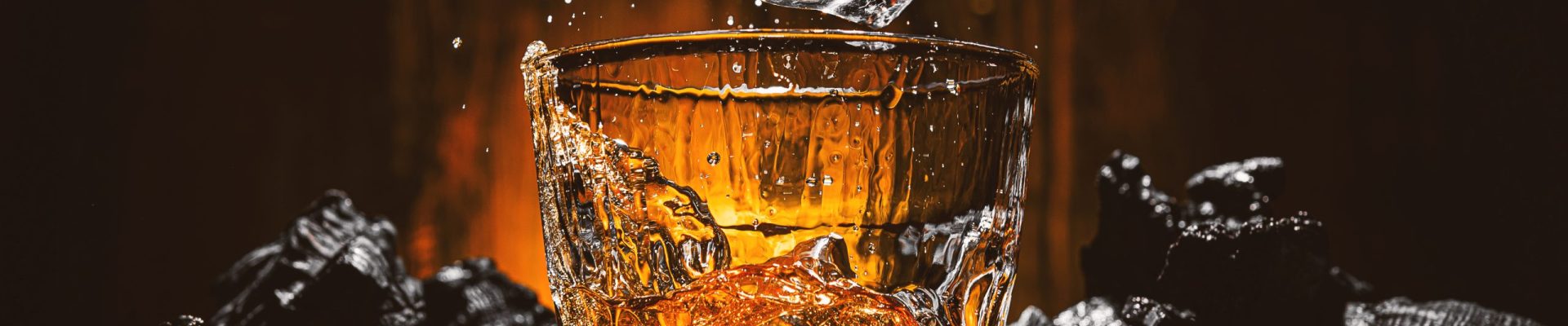 ice cubes fall into a glass with a brown alcoholic drink. splashes from falling ice fly in different directions