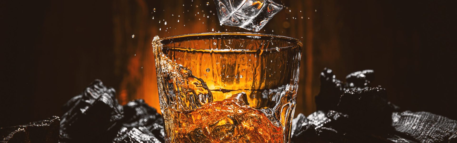ice cubes fall into a glass with a brown alcoholic drink ice cubes fall into a glass with a brown alcoholic drink. splashes from falling ice fly in different directions