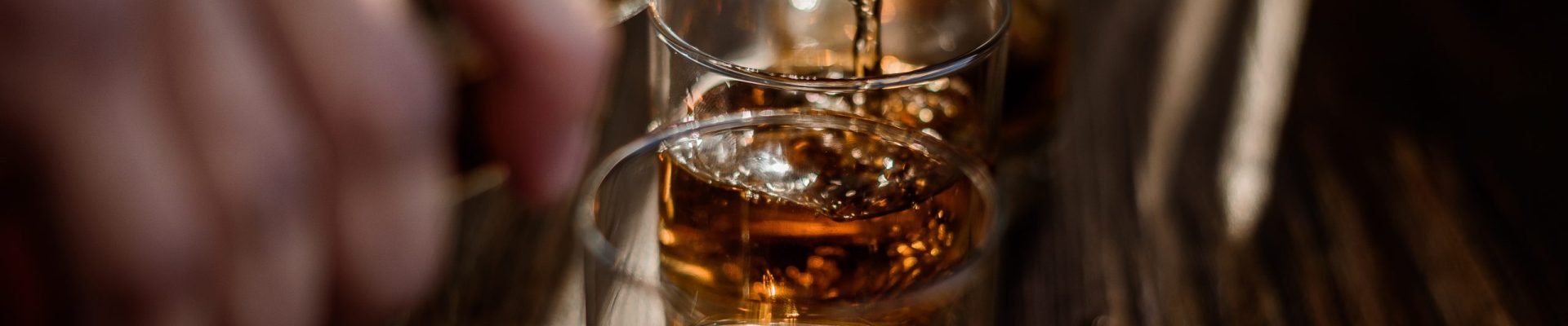 Pouring strong alcohol drink into the glasses which are on the wooden table