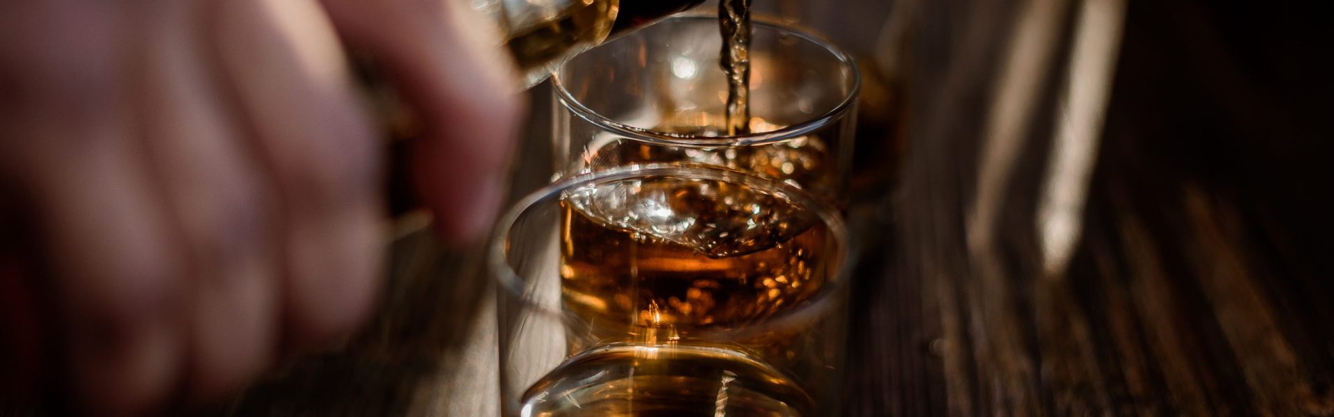 Pouring strong alcohol drink into the glasses which are on the w Pouring strong alcohol drink into the glasses which are on the wooden table